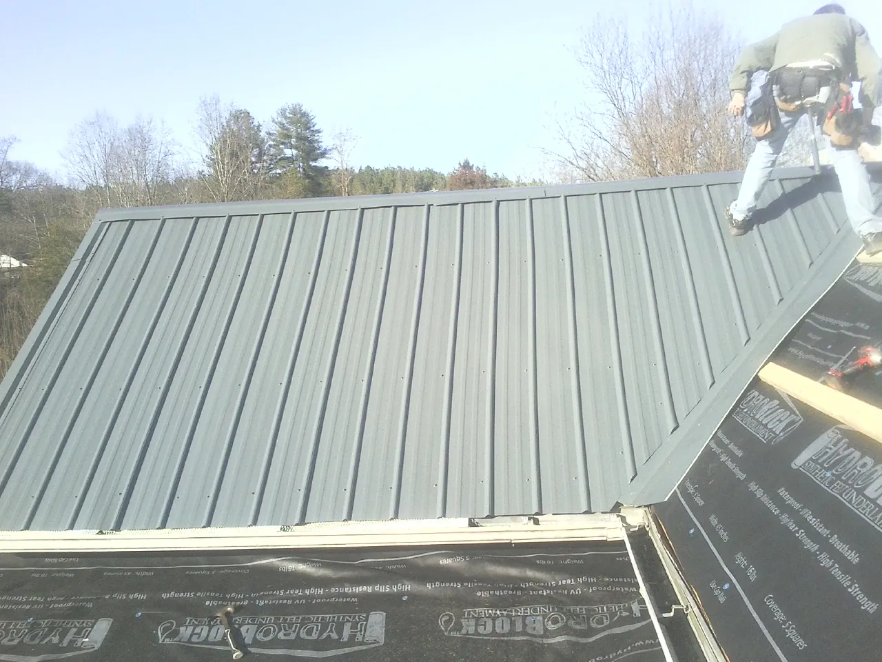 Crew installing dark green standing seam panels over synthetic underlayment in Butler