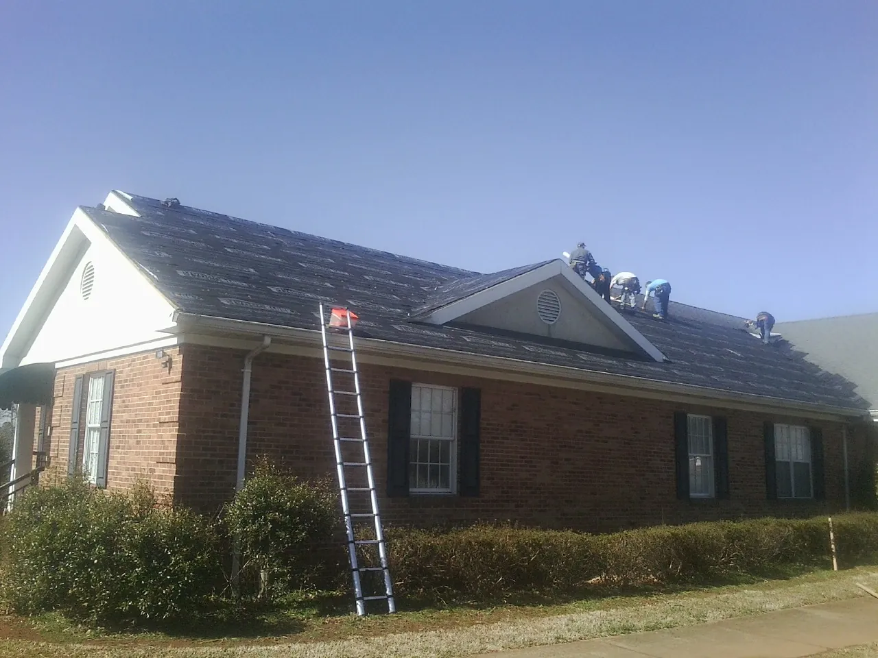 Crew tearing shingles off a brick ranch roof with a ladder set — Metal Roof Repair work by our crew in Butler
